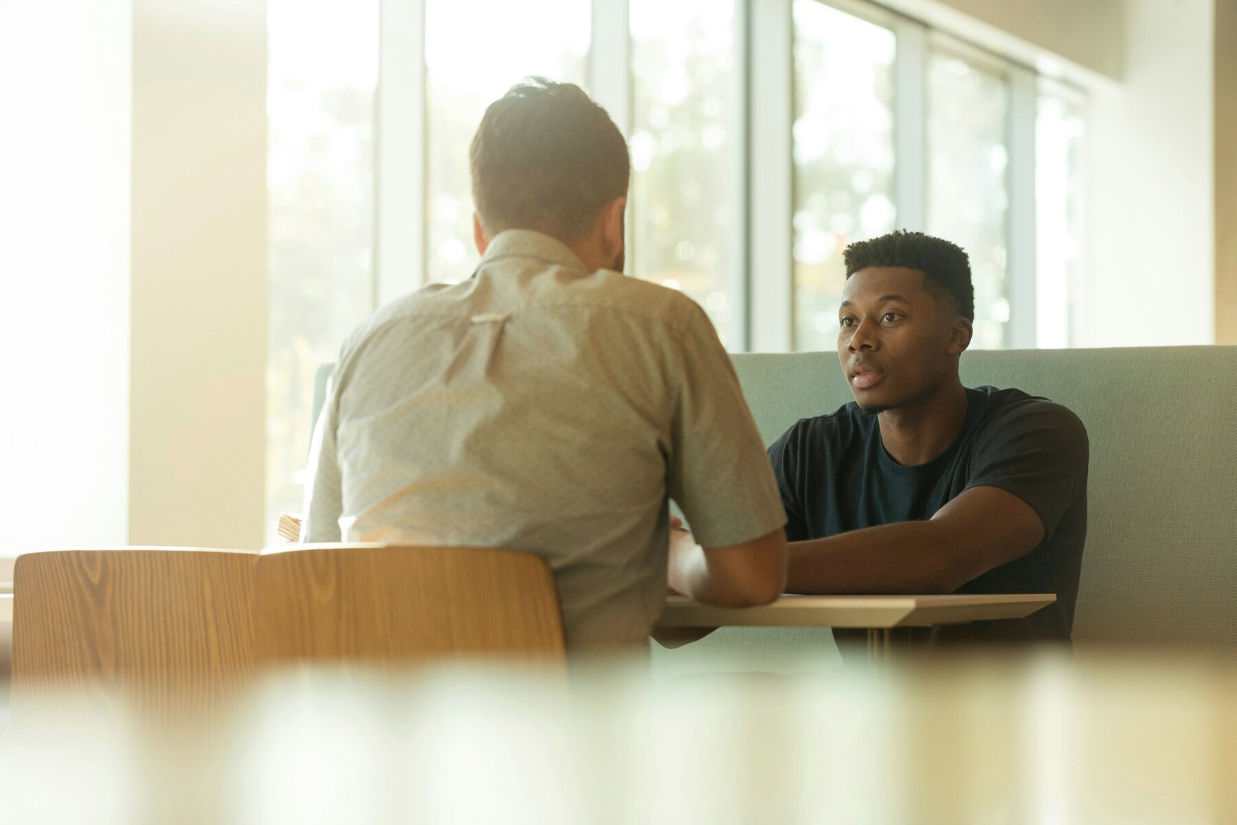 Two professionals speaking across a table in a bright workspace