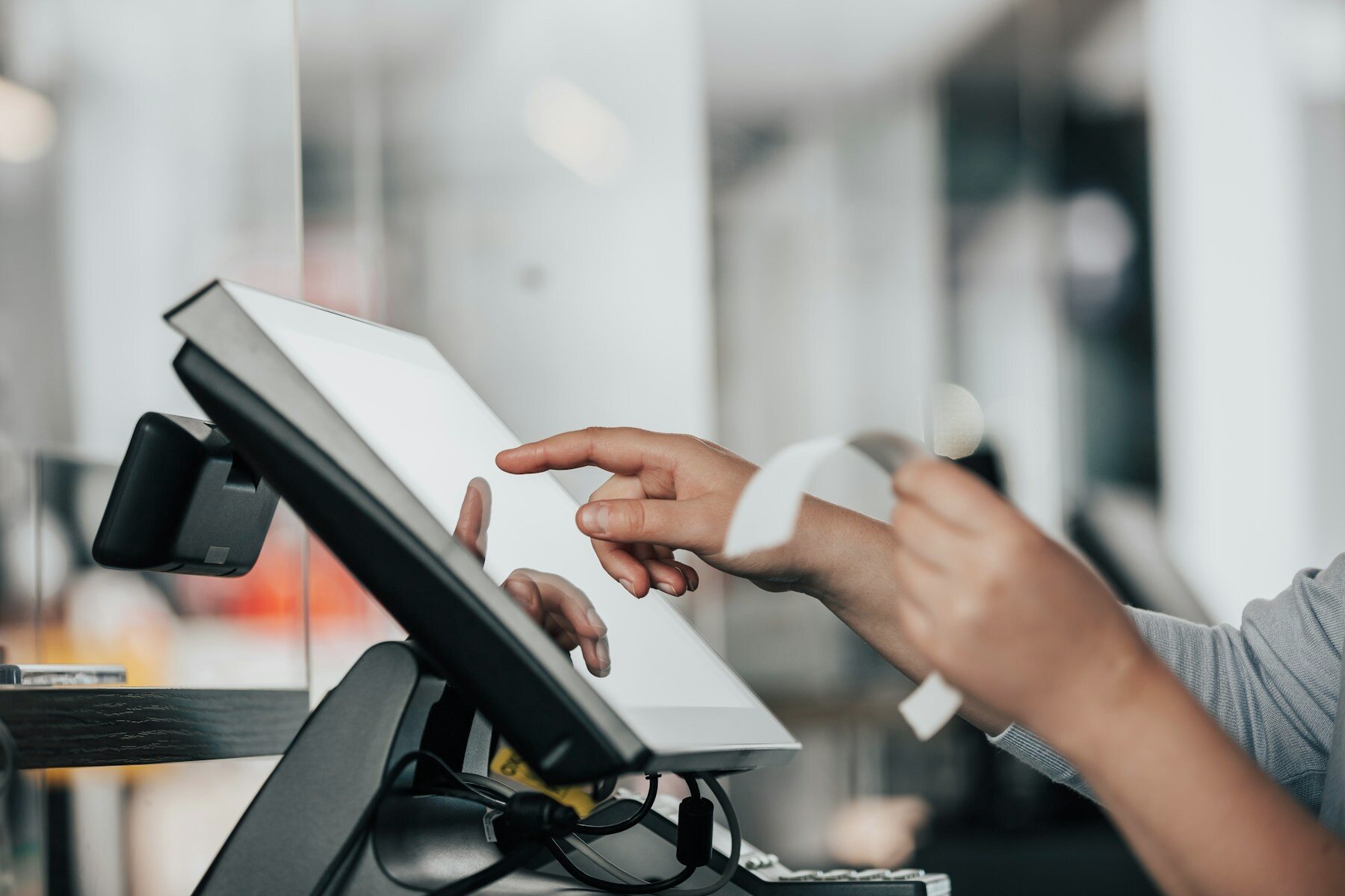 Hands operating a point-of-sale touchscreen beside a receipt roll
